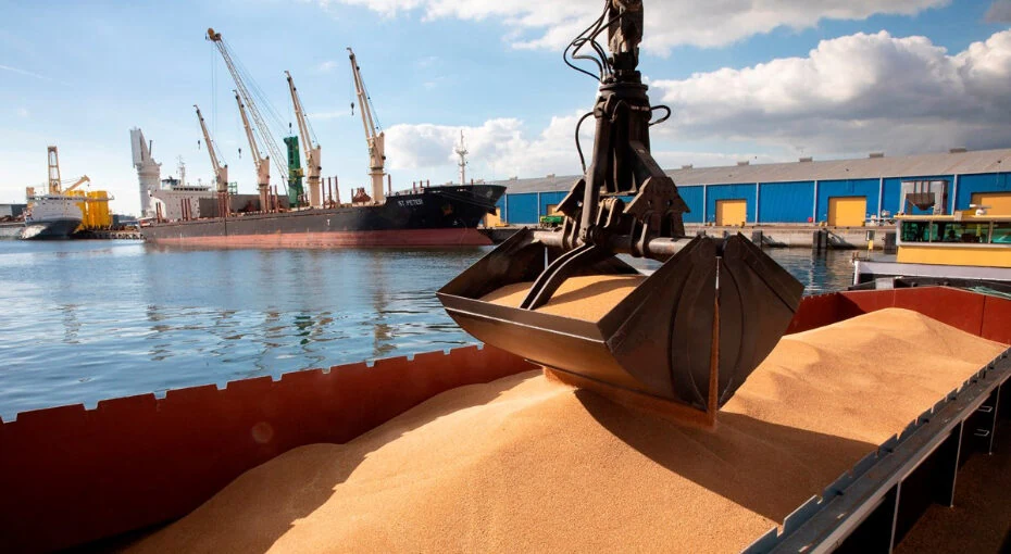 A crane grab handling bulk grain cargo alongside a vessel